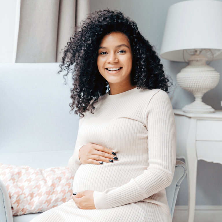 afro american adorable smiling pregnant lady beige dress sits white armchair 1